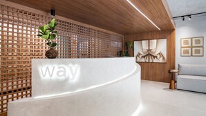 A reception desk with a wooden lattice wall, a potted plant, and framed artwork. - Way Bossa por Carpediem (João Pessoa)