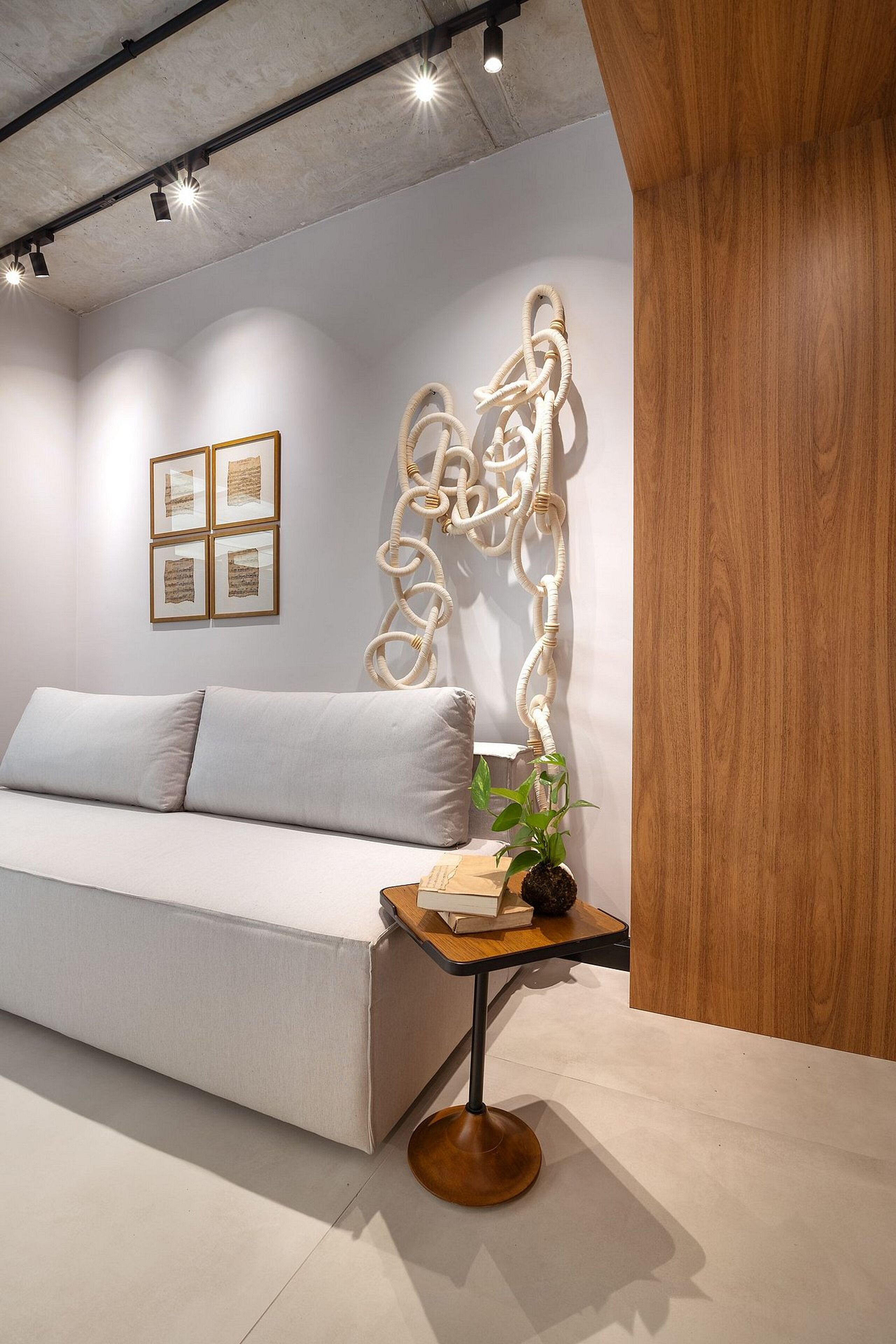 A modern bedroom with a sofa, a wooden sideboard, a wall-mounted abstract sculpture, and framed pictures.