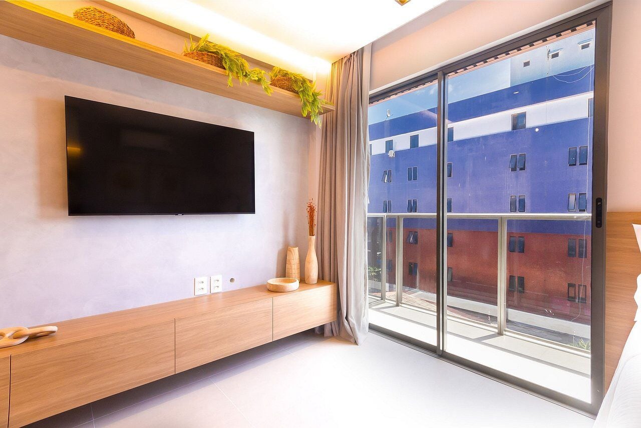 Una habitación moderna con un televisor grande, una consola de madera y un ventanal con vistas a edificios.