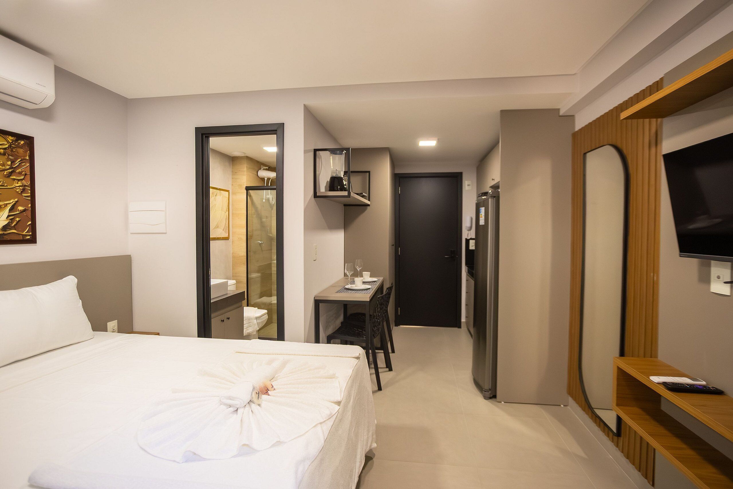 A hotel room with a bed, a desk, a mirror, a television, and a shower area.