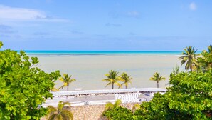 A beach view with palm trees, a clear sky, and a building with 'VIA ANO' signage. - Way Bossa por Carpediem (João Pessoa)