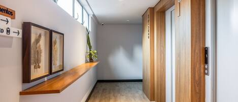 Un couloir doté d’un plancher en bois, avec des œuvres d’art encadrées exposées sur une étagère, et un panneau indiquant une direction.