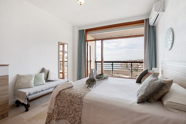 A hotel room with a bed, a sofa, a balcony with a view, and an air conditioning unit.