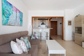 A living room with a sofa, a coffee table, and a kitchen area with a bar stool.