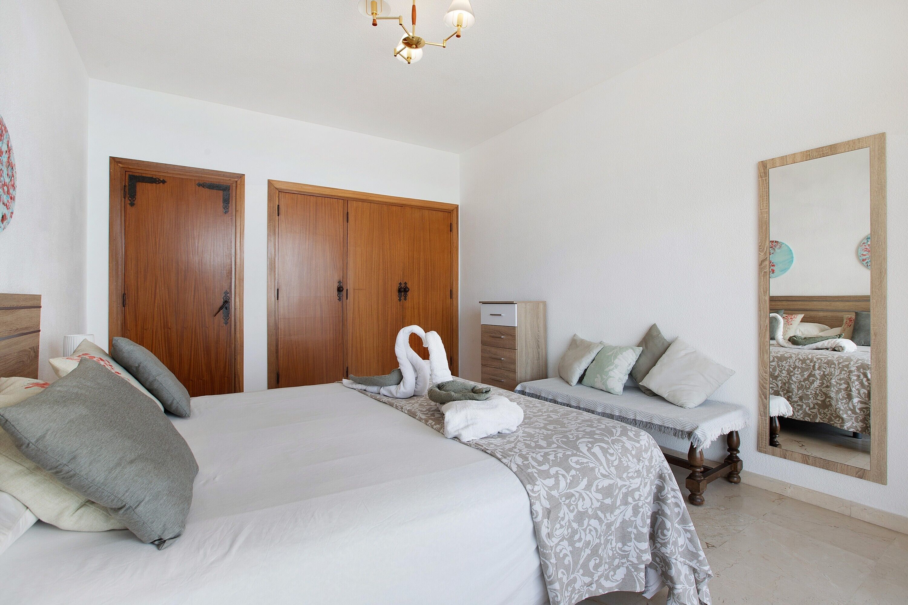 Une chambre d’hôtel avec un grand lit, deux armoires, une table de chevet, un miroir et un luminaire au plafond.