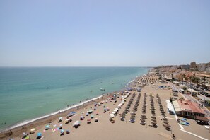 A beach with rows of umbrellas and beach chairs, a clear sky, and a calm sea.