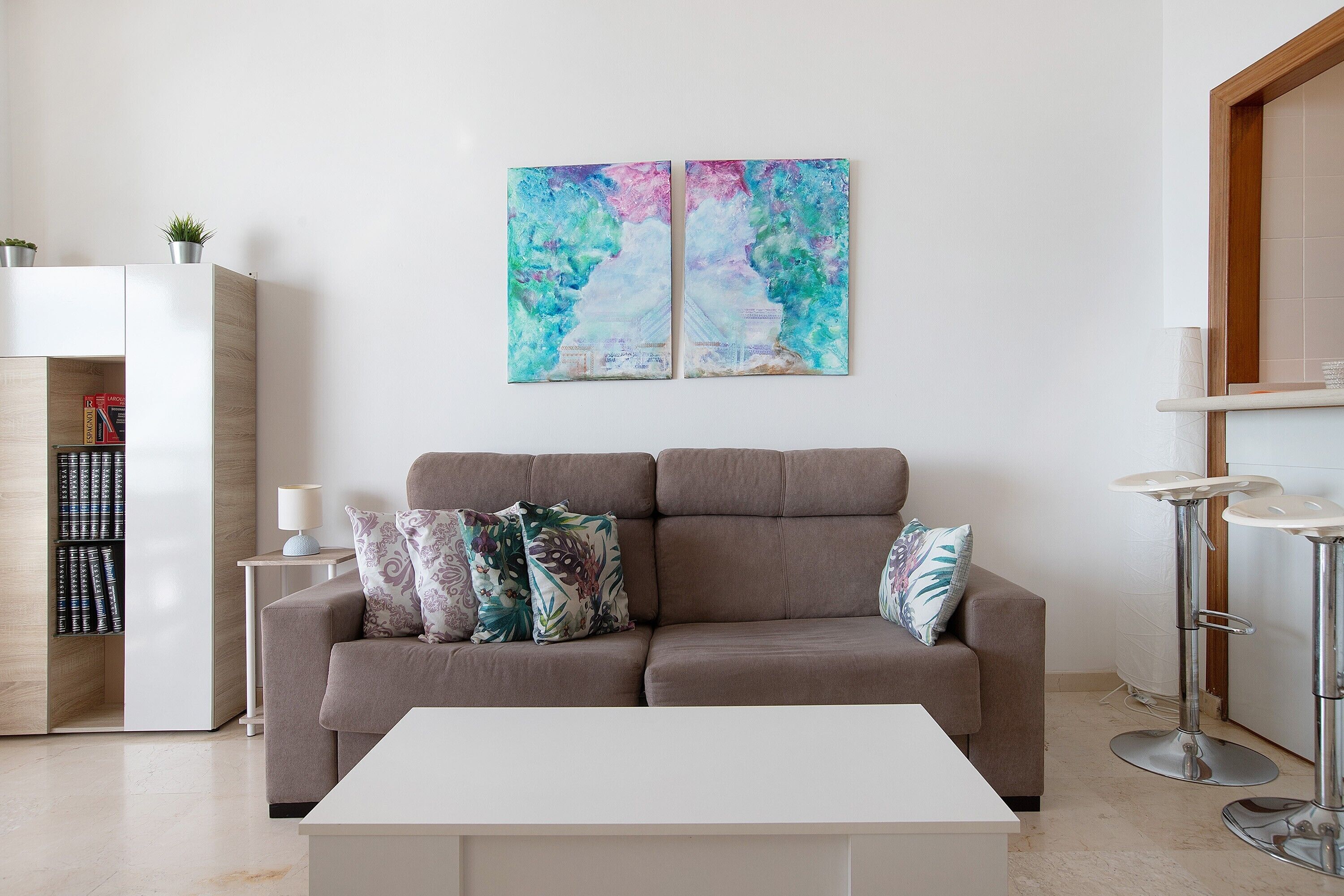 A modern living room with a sofa, a coffee table, a bookshelf, and two abstract paintings on the wall.
