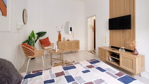 A modern living room with a flat-screen TV, a wooden cabinet, a round table, and a patterned rug.