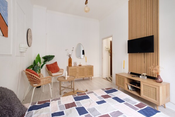 A modern living room with a flat-screen TV, a wooden cabinet, a round table, and a patterned rug.