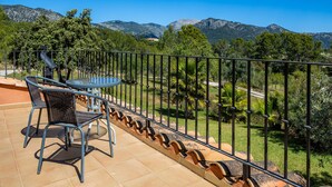 Une terrasse avec une table et des chaises, une rambarde en métal et une vue sur les montagnes.