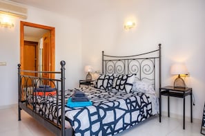 Un dormitorio ordenado con una cama de estructura metálica, dos mesitas de noche con lámparas y una puerta de madera.