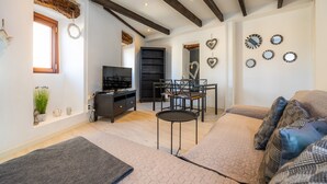A modern living room with a sofa, a small round table, a TV, and a dining area with chairs. - Apartment 'Can Roses' with Private Terrace, Wi-Fi and Air Conditioning (Moscari)