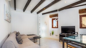 A modern living room with a sofa, TV, glass table, and wooden beams. - Apartment 'Can Roses' with Private Terrace, Wi-Fi and Air Conditioning (Moscari)