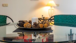 Una mesa de vidrio redonda con un centro decorativo, dos sillas tapizadas en verde, una lámpara y una pared con una obra de arte roja y negra.