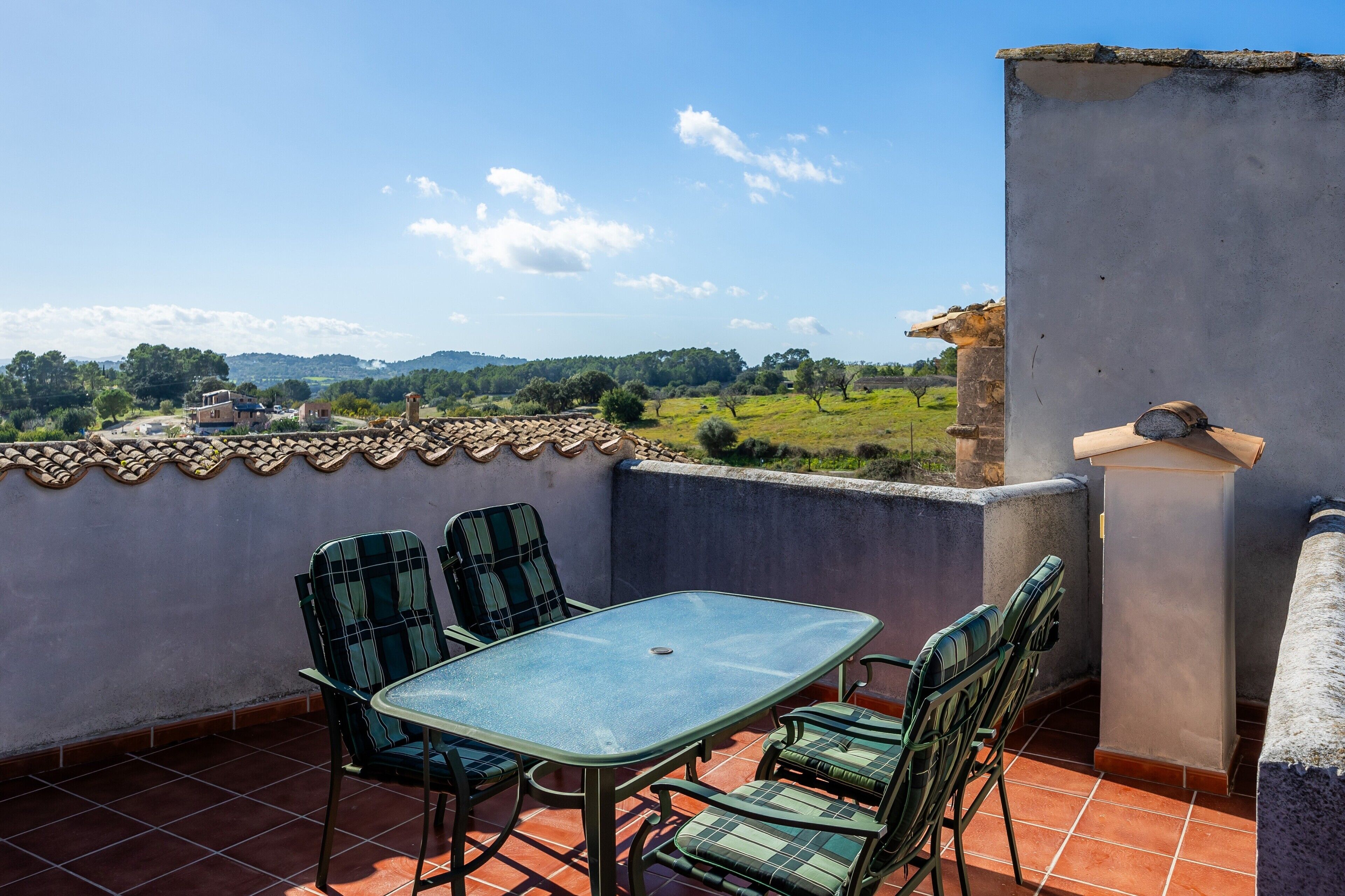 Una terraza con una mesa y sillas, vistas al campo y un muro de piedra.