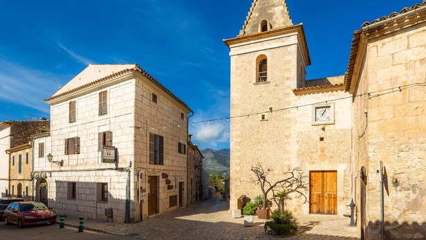 Una calle histórica con edificios de piedra, una torre de iglesia y un camino adoquinado.