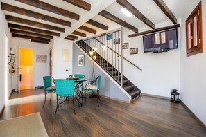 A dining area with a staircase, wooden beams, a TV, and a small table with chairs. - Edificio duplex can roses (Moscari)