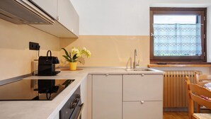 A compact kitchen with a built-in stove, a sink, and a window with a curtain. - Holiday Home 'Le Cré Appartamento 2' with Mountain View, Shared Garden and Wi-Fi (Introd)