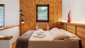 A bedroom with wooden paneling, a bed with towels, a window, and a lamp. - Holiday Home 'Le Cré Appartamento 2' with Mountain View, Shared Garden and Wi-Fi (Introd)