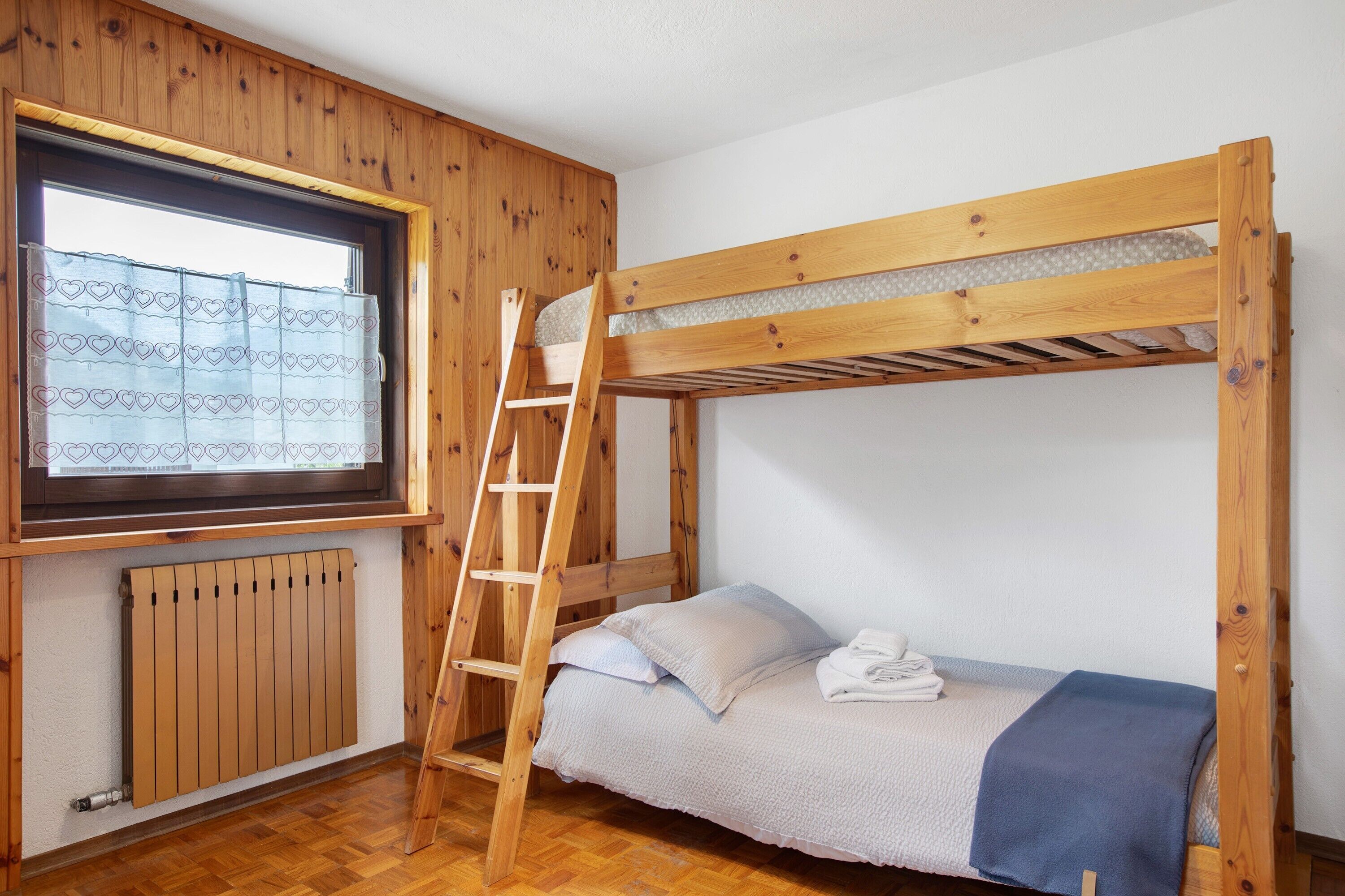 Un lit superposé avec une échelle en bois, une fenêtre avec des rideaux à motifs et un radiateur.
