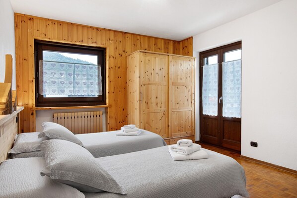 Une chambre avec deux lits, des boiseries, une fenêtre donnant sur un beau paysage et une armoire.