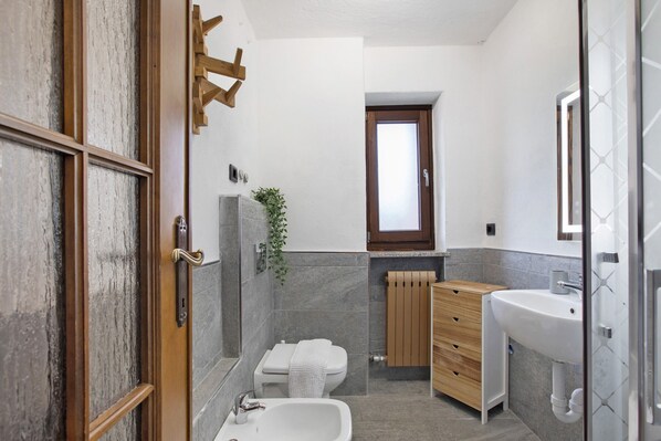 A bathroom with a wooden door, a white sink, a wooden vanity, a white toilet, and a shower area.