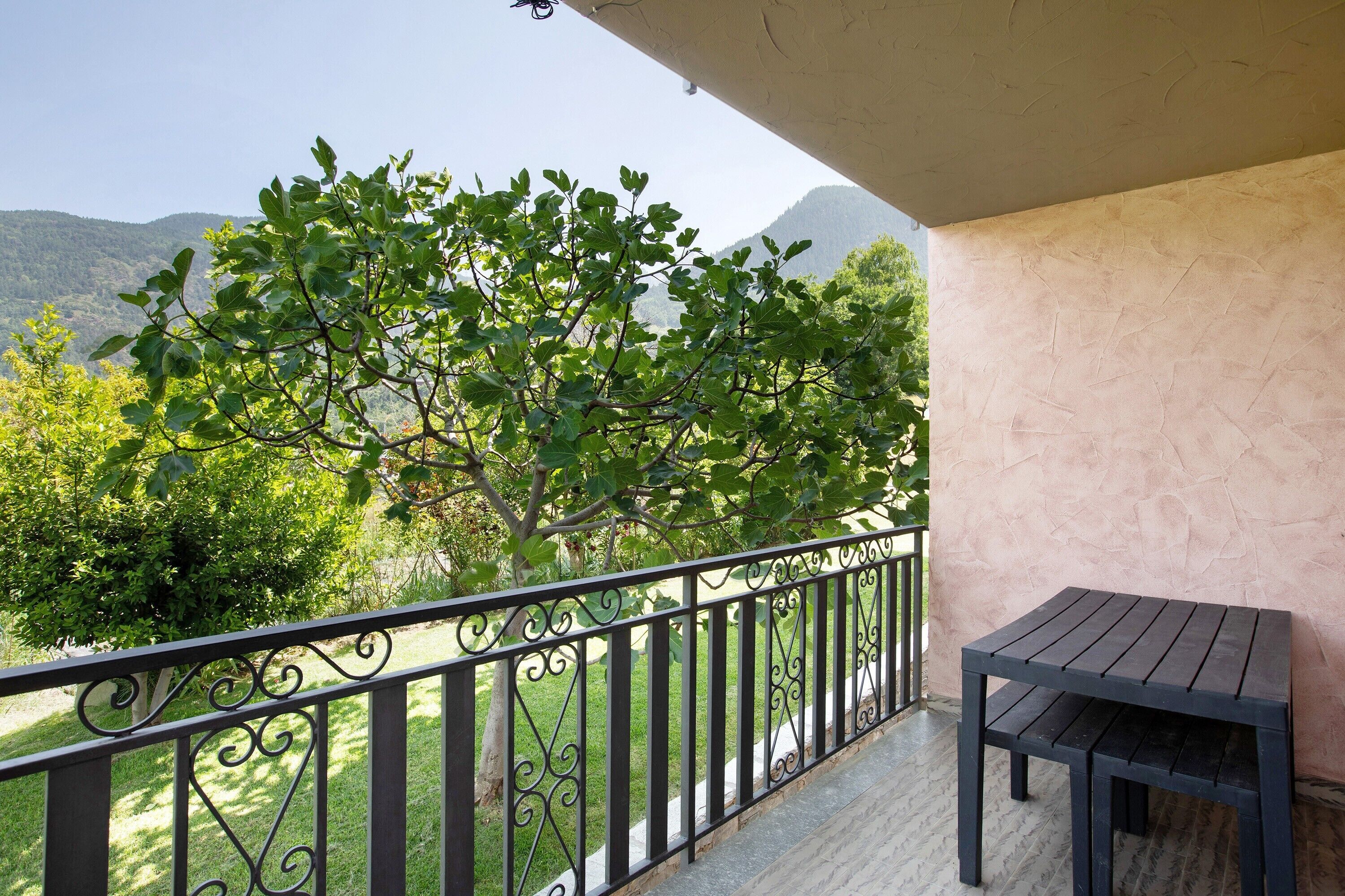 A balcony with a view of mountains, a table, and a decorative fence.