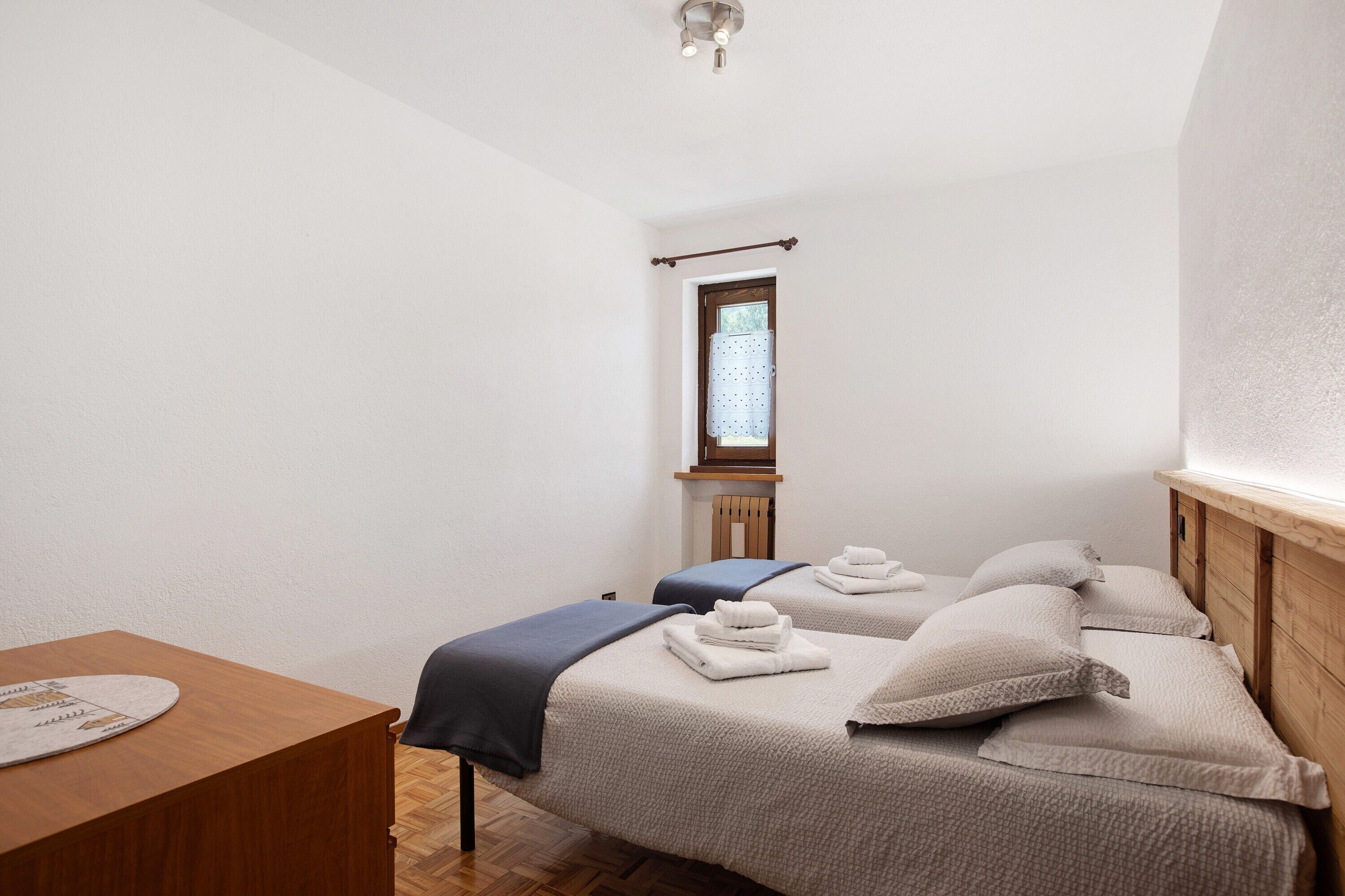 Una stanza con due letti, un tavolo in legno e una finestra con tenda.
