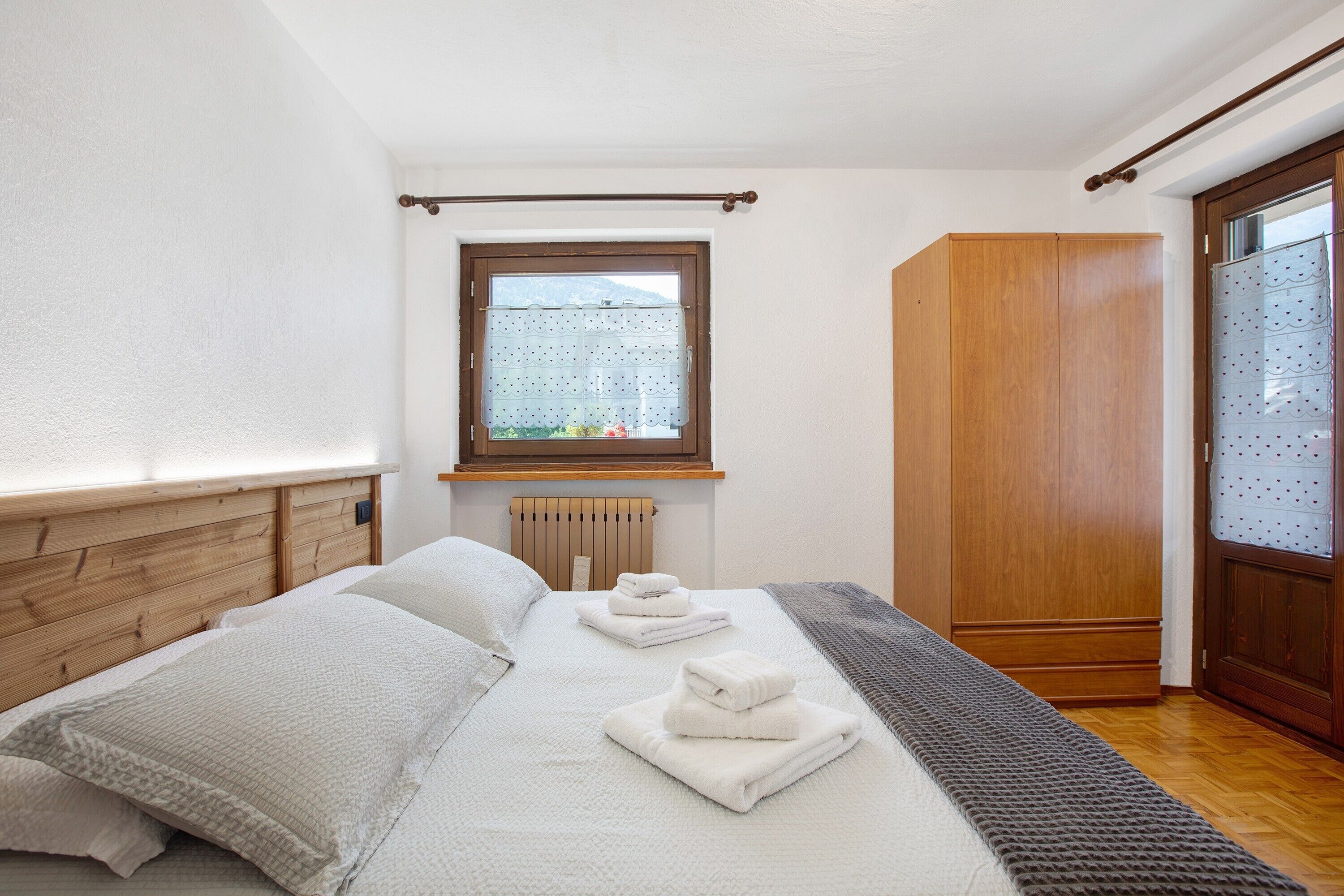 Un dormitorio con cabecera de madera, ventana con vistas, armario y toallas ordenadas sobre la cama.