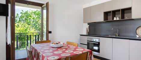 A kitchen with a dining table, cabinets, and a view of greenery outside.
