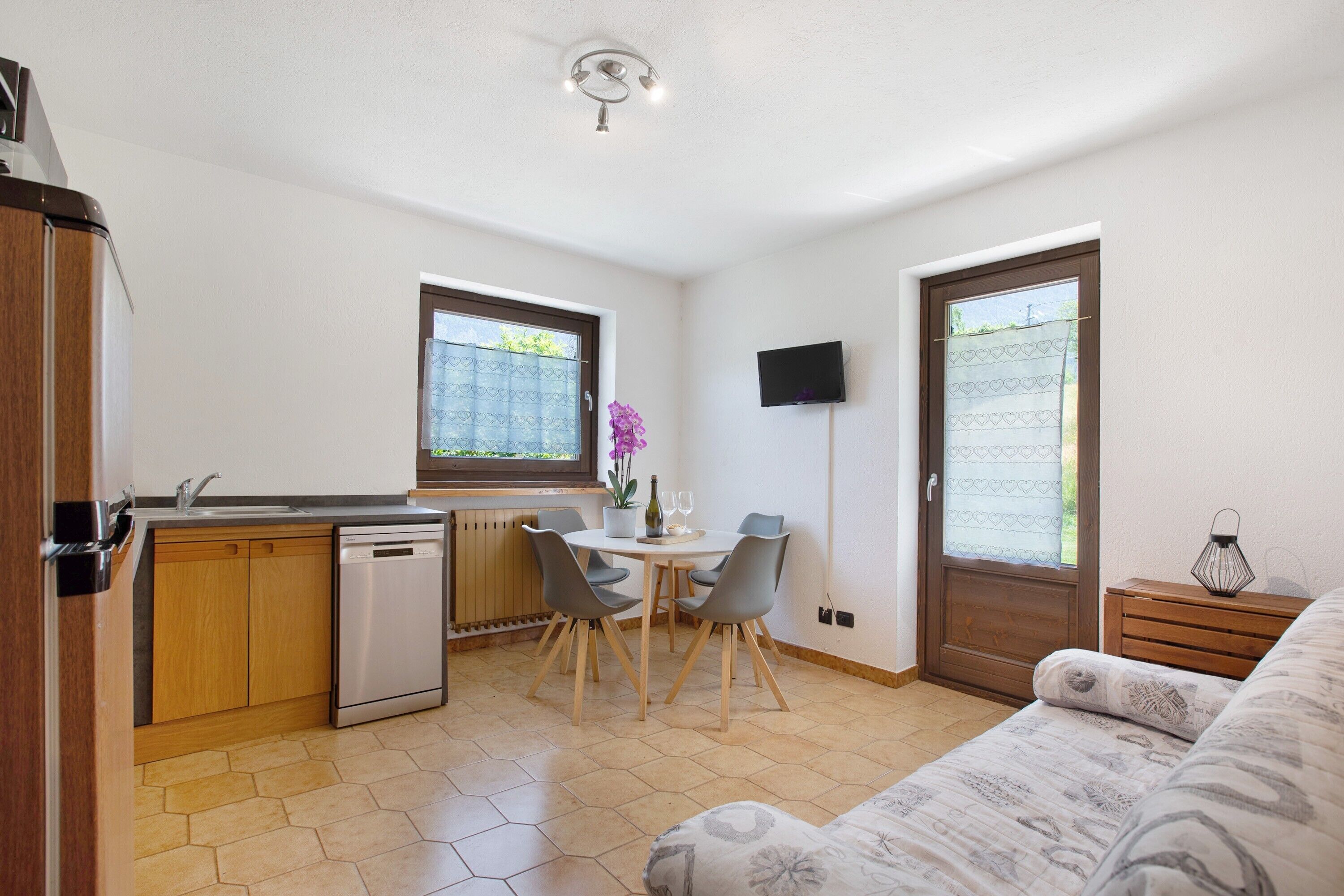 Cocina compacta con lavavajillas, una mesa de comedor con sillas, televisor montado en la pared y sofá en la sala.