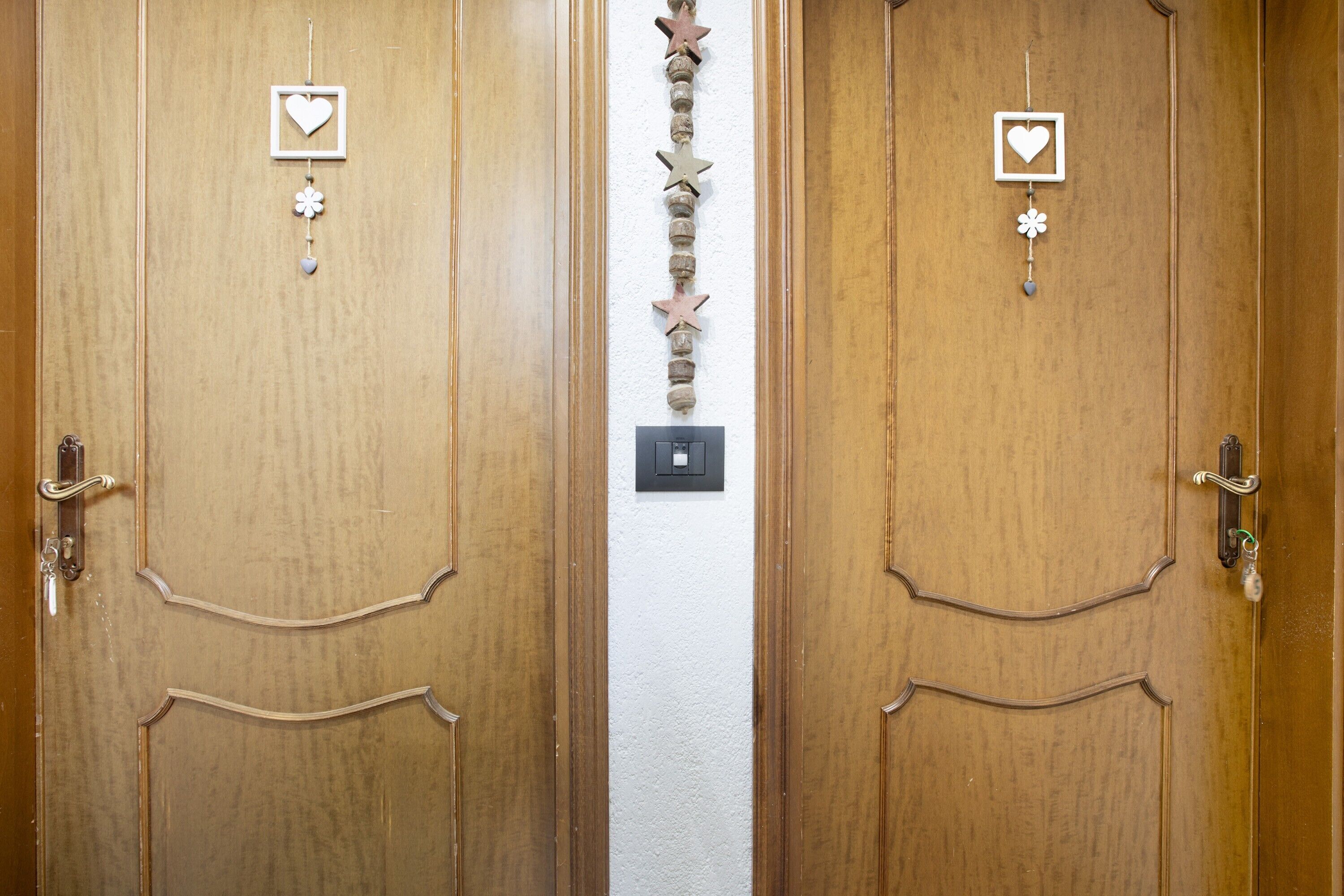 Dos puertas de madera con un hilo vertical de adornos y un interruptor de luz entre ellas.