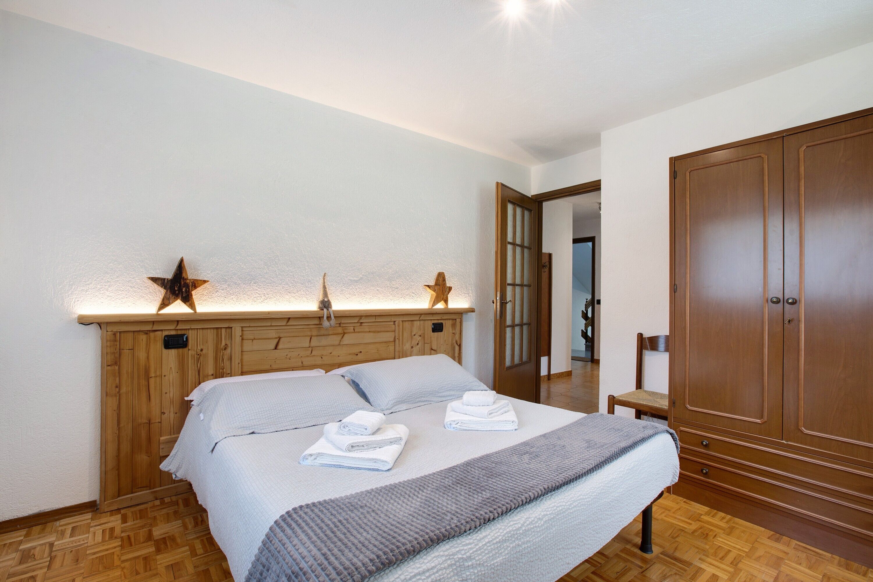 A bedroom with a wooden headboard, a bed with white linens, a bedside table, and a wardrobe.