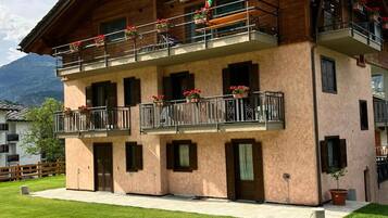 Un edificio a più piani con balconi, facciata in legno e un prato davanti.