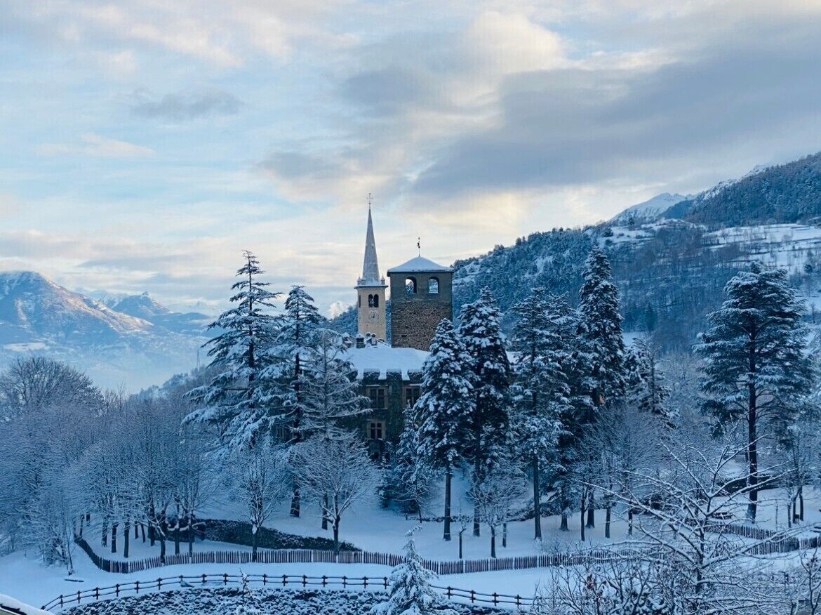 A snow-covered landscape with a church and surrounding trees.