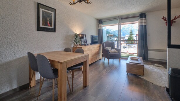 A dining area with a wooden table and chairs, a chandelier, a television, and a view of mountains through large windows. - Studio "2 Alpes" with Mountain View, Private Terrace, and Balcony (Les Deux Alpes)