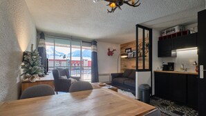A modern living room with a wooden dining table, a sofa, and a small kitchen area with a refrigerator and cabinets. - Studio "2 Alpes" with Mountain View, Private Terrace, and Balcony (Les Deux Alpes)