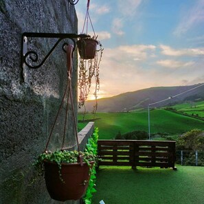 A stone wall with hanging planters and a view of a green field at sunset.