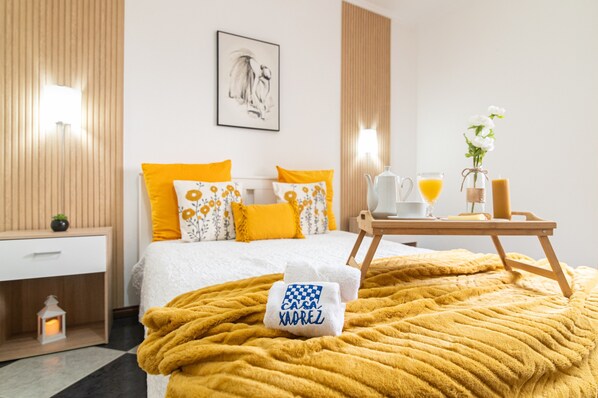 A hotel room with a bed, a bedside table, a nightstand, a lamp, a framed picture on the wall, a tray with a coffee pot, a glass of orange juice, and a towel with a logo.