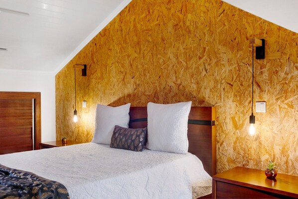 A bedroom with a sloped ceiling, wooden wall paneling, a bed with white bedding, two bedside tables with lamps, and a small plant on one table.