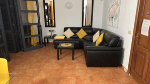 A living room with a black leather sofa, a small coffee table, and a yellow chair. There is a wooden door and a mirror on the wall. - 2 Bedroom, 2 Bathroom Villa in Great Location (Playa Blanca)