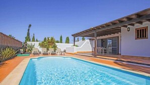A swimming pool with a pergola and outdoor seating, surrounded by a white building and palm trees. - 2 Bedroom, 2 Bathroom Villa in Great Location (Playa Blanca)