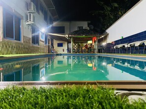 A swimming pool with a clear water surface, surrounded by a wooden fence and a grassy area. - Luxurious Ten-Bedroom Lodge Apartment (Sekondi-Takoradi)