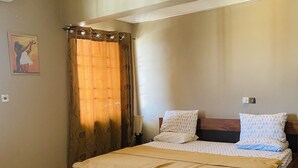 Ein Schlafzimmer mit einem hölzernen Bett, beigen Wänden, einem weißen Teppich und einem braunen Vorhang.