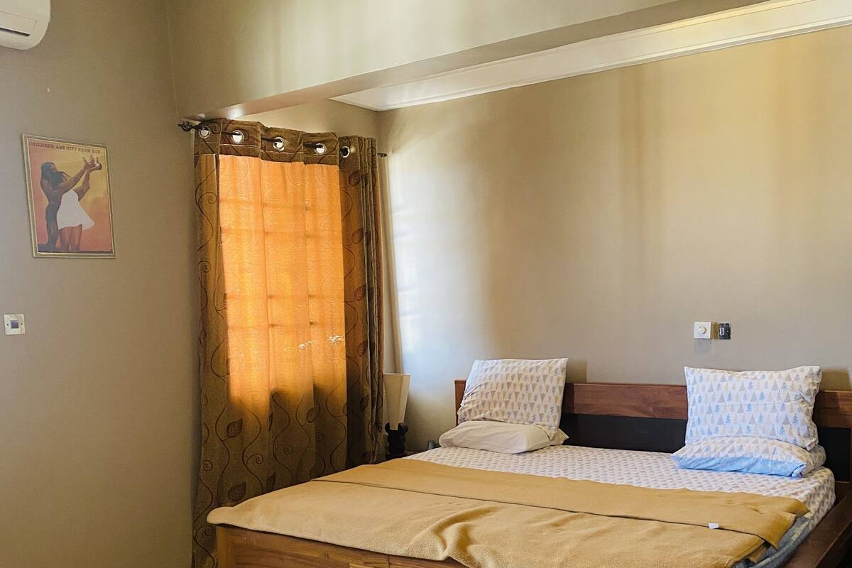 A bedroom with a wooden bed, beige walls, a white rug, and a brown curtain.