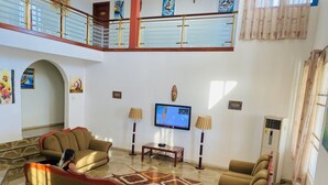 Ein geräumiges Wohnzimmer mit hoher Decke, einem Balkon und einem Fernseher.