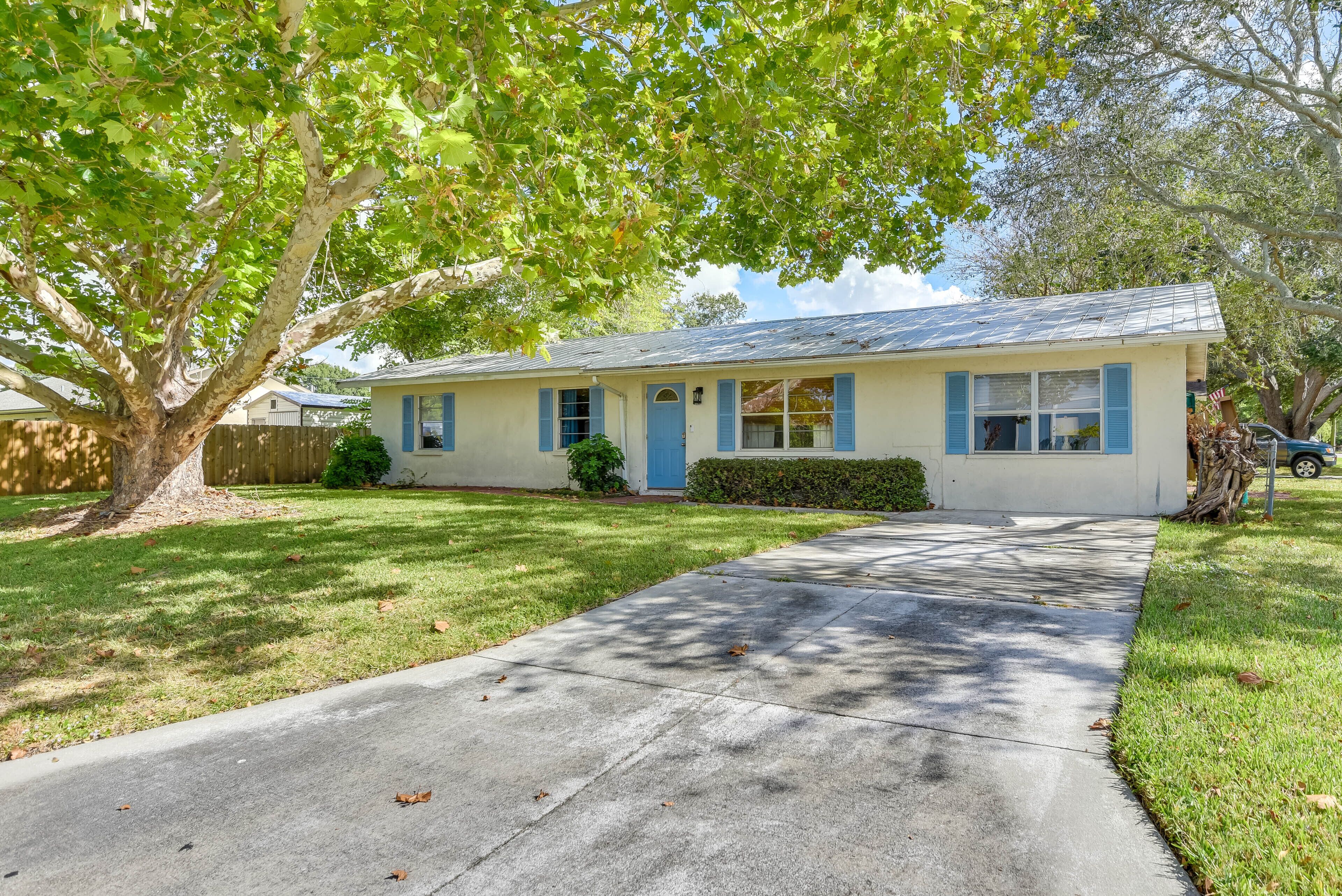 A single-story house with a front yard, a driveway, and a tree.