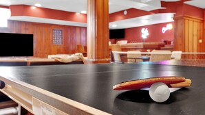 Una mesa de ping pong con una paleta y una pelota en una habitación con paredes de madera y un letrero de neón.