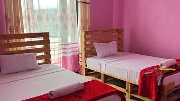 Une chambre avec deux lits en bois, chacun doté d’un matelas blanc et d’une couverture rouge. Les murs de la chambre sont peints en rose et il y a une fenêtre avec des rideaux à motifs.
