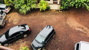 A parking area with two cars and a white van, surrounded by greenery and a tiled building facade. - Kilimanjaro Smiley Inn (Moshi)